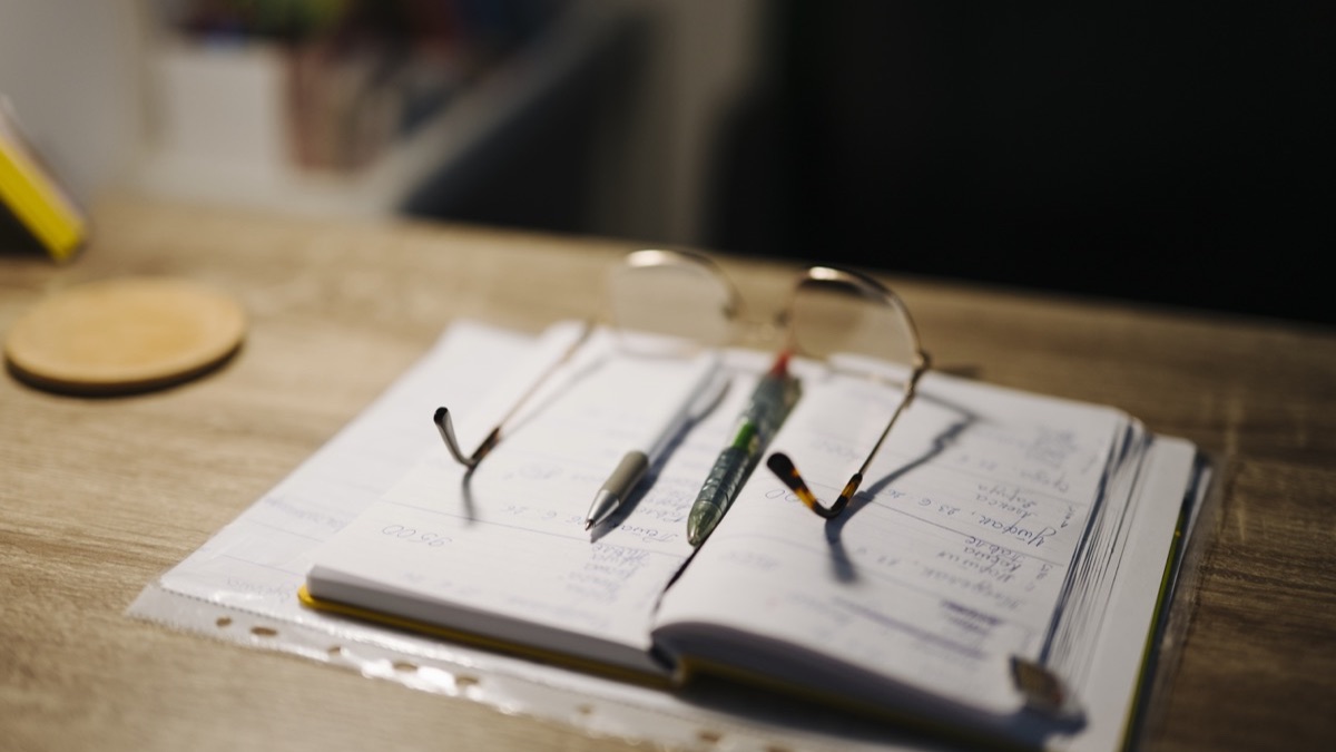 An open notebook with pens and glasses on a study desk